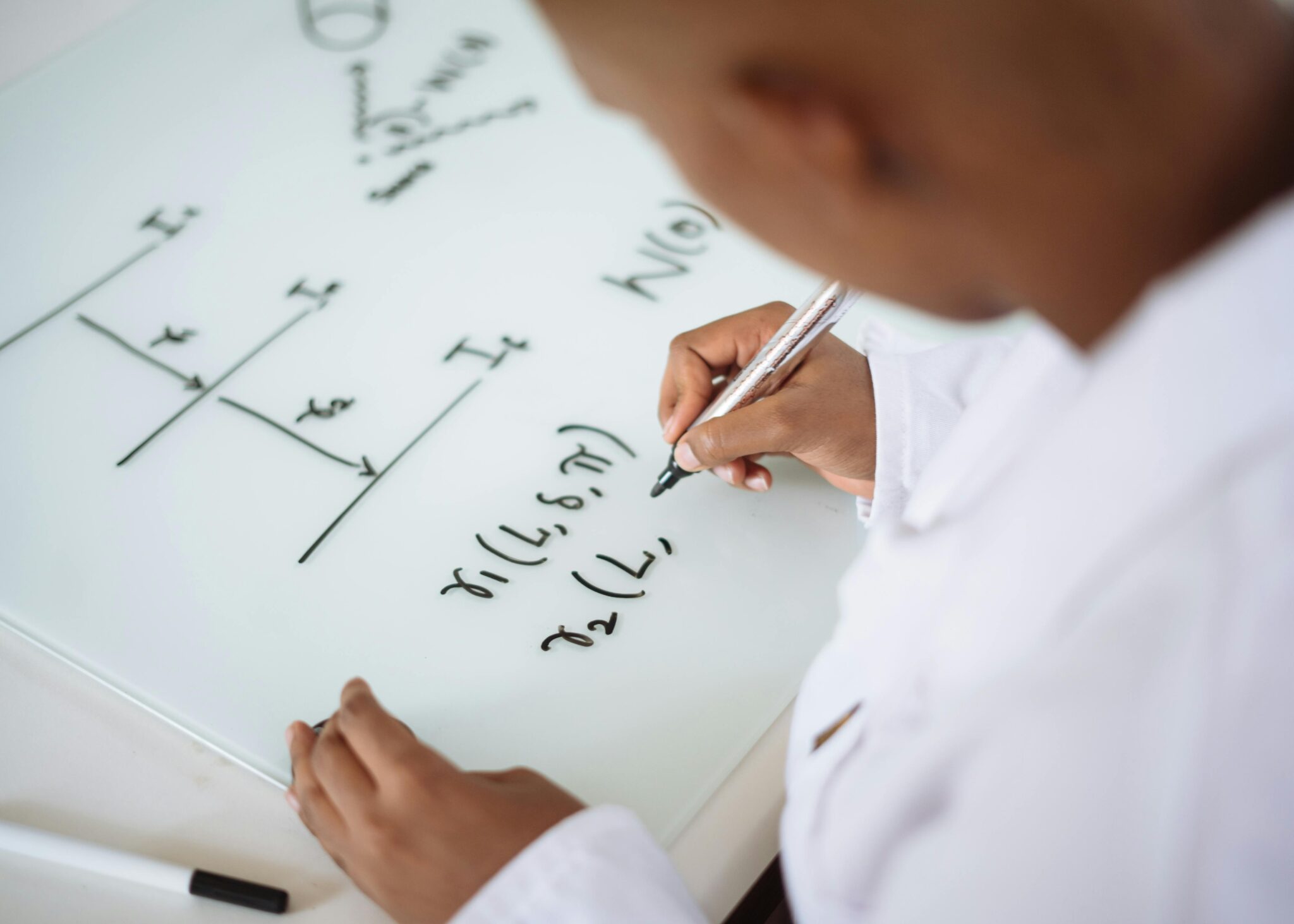 From above anonymous ethnic student wearing uniform and solving problem in chemistry while writing formula on white table in lab